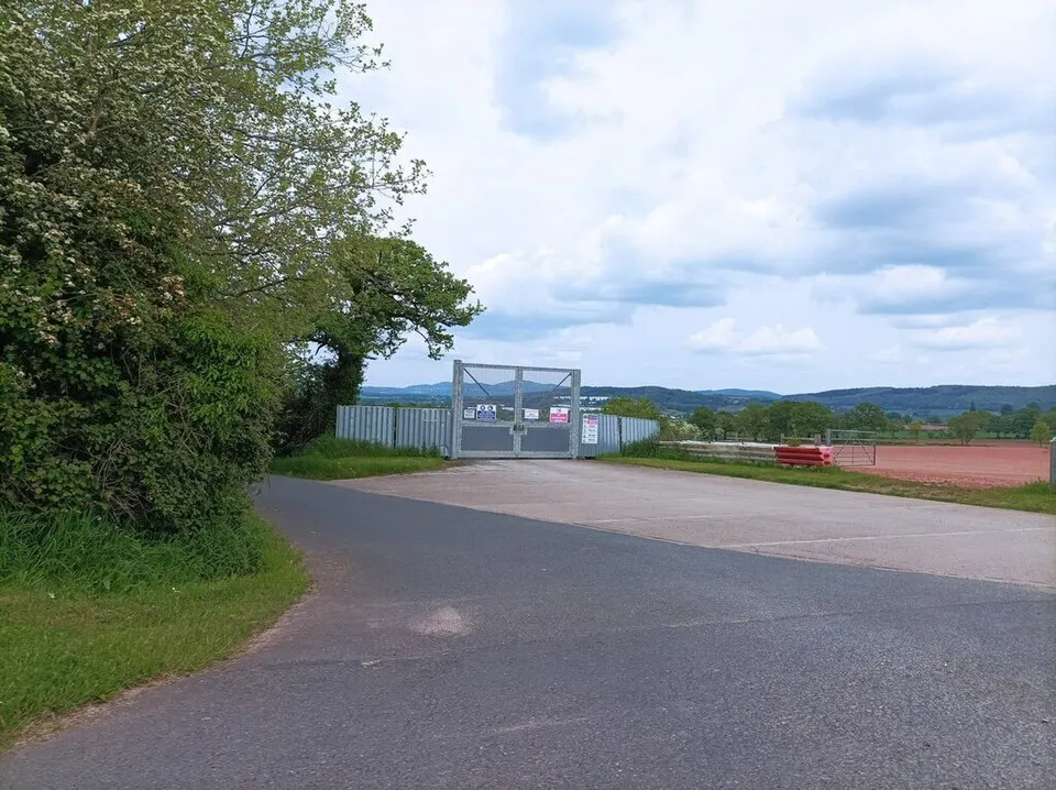 Paved entry road ending at a wide security gate and fence line